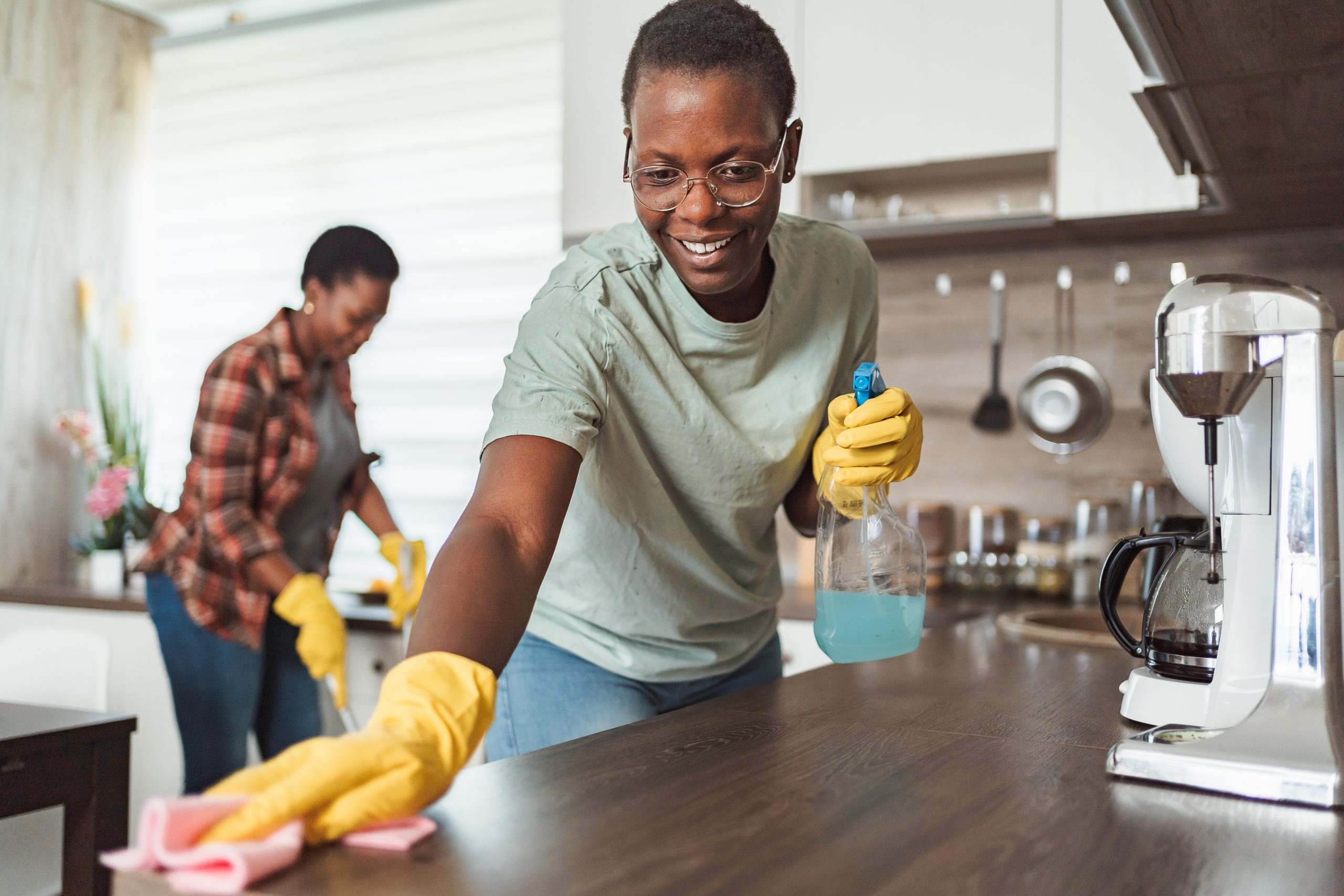 Two smiling african housekeepers wearing gloves and cleaning kitchen counter and floor